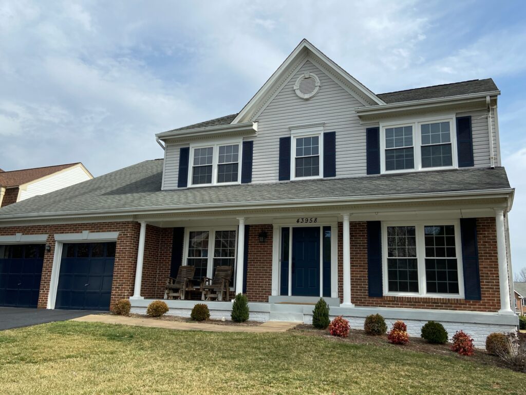 Two-story white lap-sided colonial with brick base, blue front door, double-hung windows with shutters, and a covered porch.