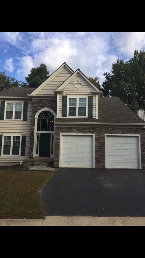 Two-story tan home with stone accent, palladian-style entry window, green door, and two-car garage.
