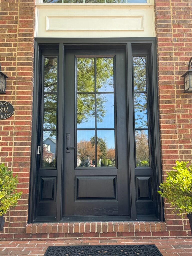 Black craftsman 6-lite front entry door with full-height sidelights and transom on a brick home.