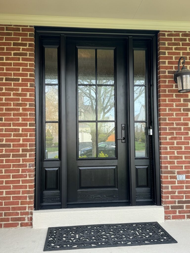 Black craftsman-style front entry door with 6-lite glass and sidelights on a brick home.