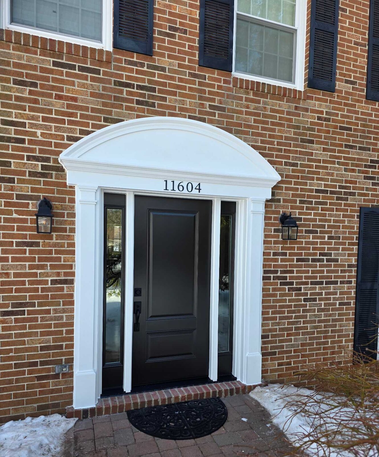 New black entry door and arched portico on a brick colonial after replacement