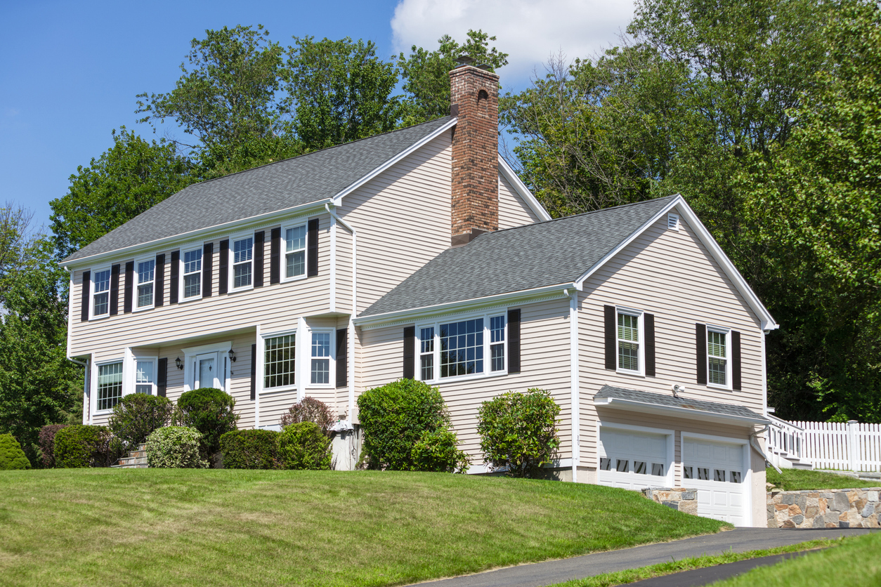 Colonial with light siding, brick chimney, and mature trees